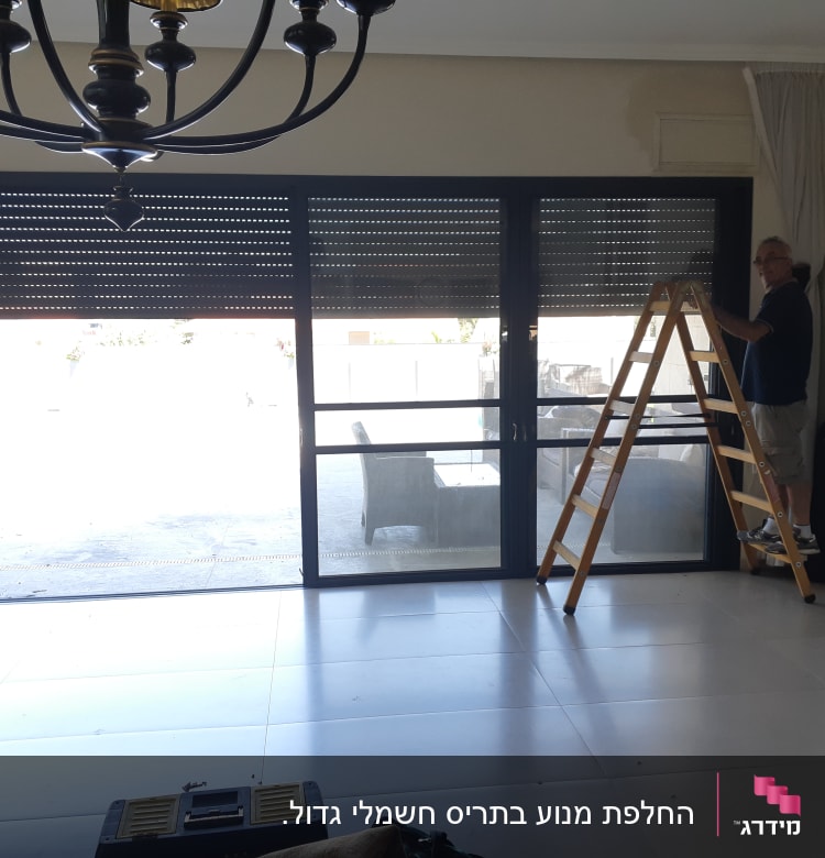 אדם על סולם מתקין תריסים בחלון גדול